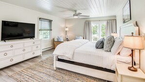A bedroom with a bed, a TV, a ceiling fan, a nightstand, and a window with curtains.