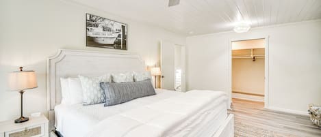A bedroom with a large bed, a ceiling fan, a nightstand, a lamp, and a framed picture on the wall.