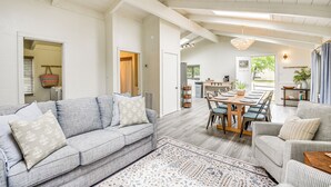 A spacious living room with a grey sofa, a patterned rug, and a dining area with a wooden table and chairs.