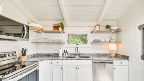 A modern kitchen with white cabinets, a built-in oven, a dishwasher, and a marble countertop.
