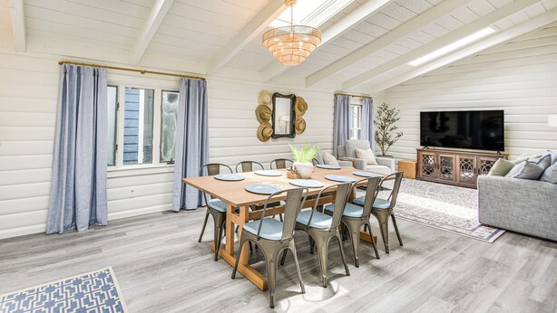 A dining area with a wooden table and chairs, a chandelier, and a television in the background.