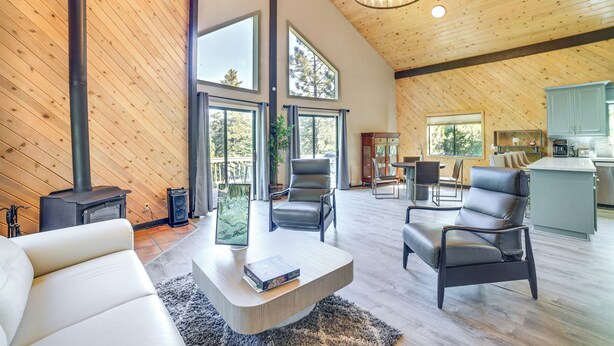 A spacious living area with a large fireplace, leather chairs, and a modern kitchen in the background. - Pine Mountain Club Cabin w/ A/C & EV Charger (Pine Mountain Club)