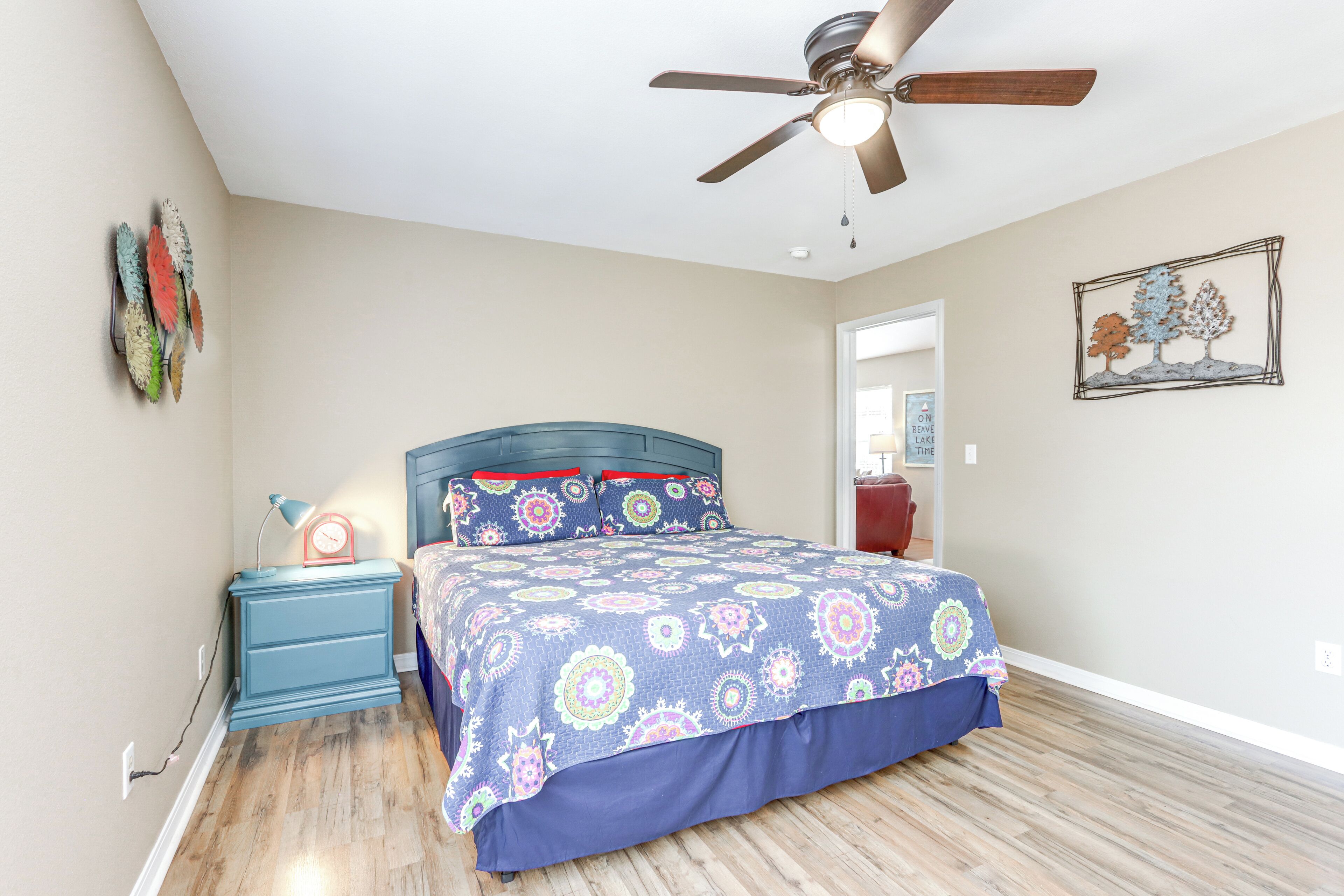 Une chambre à coucher comprenant un lit, une table de chevet, un ventilateur de plafond et un mur agrémenté d’un élément décoratif.