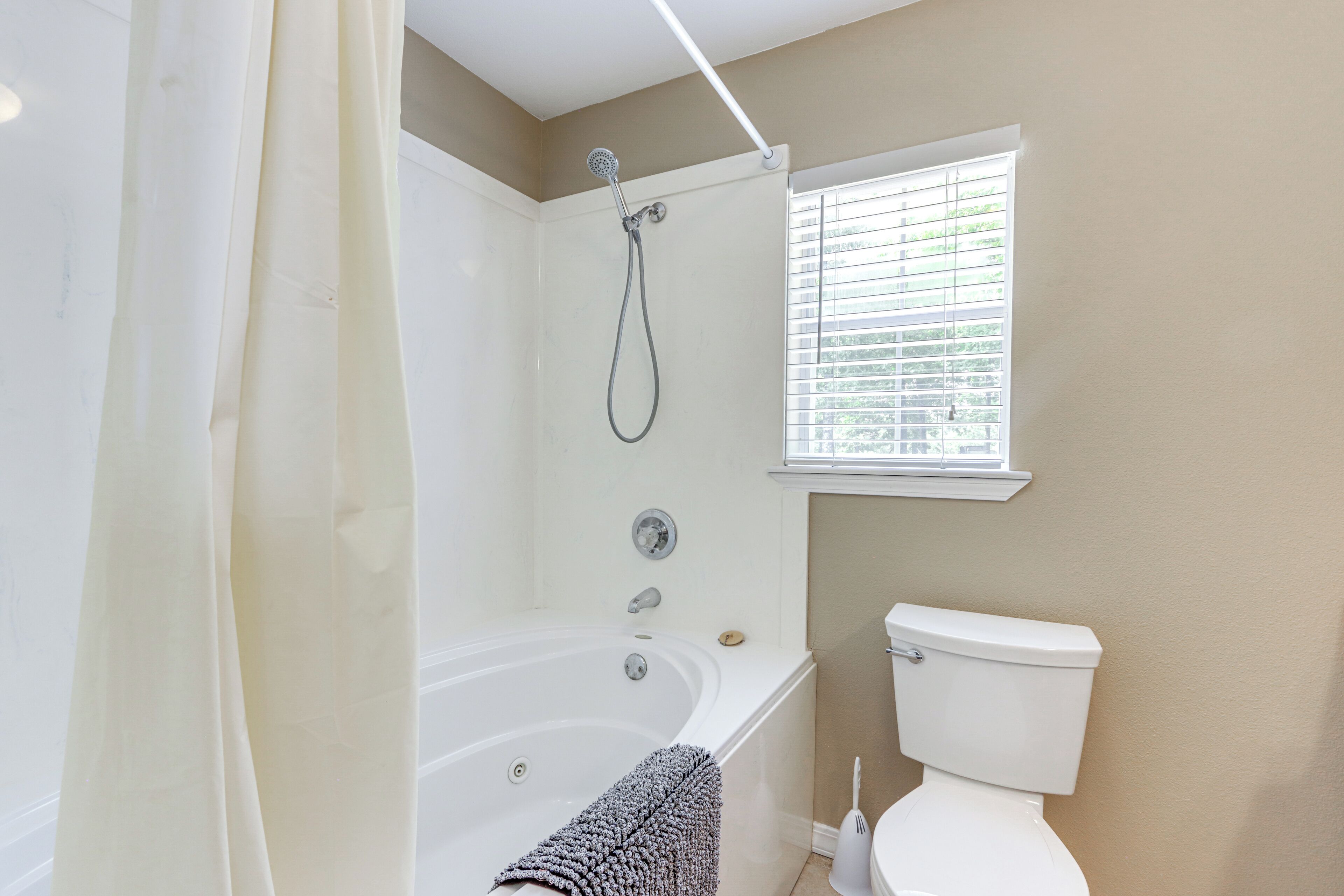 Une salle de bain avec une baignoire, des toilettes et une fenêtre avec des stores.