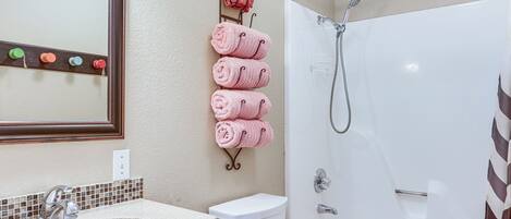 Een badkamer met een wastafel, toilet en douche. Handdoeken hangen aan een rek.