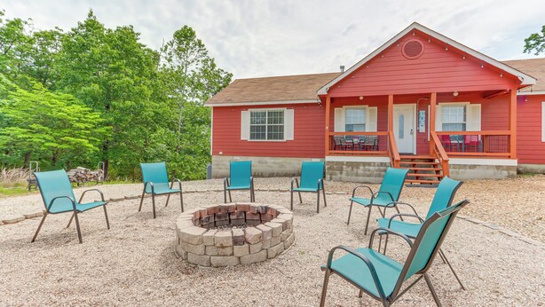 A red building with a porch and outdoor seating area with chairs and a fire pit.