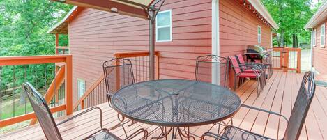 A covered outdoor deck with a metal table and chairs, a barbecue grill, and a wooden railing.