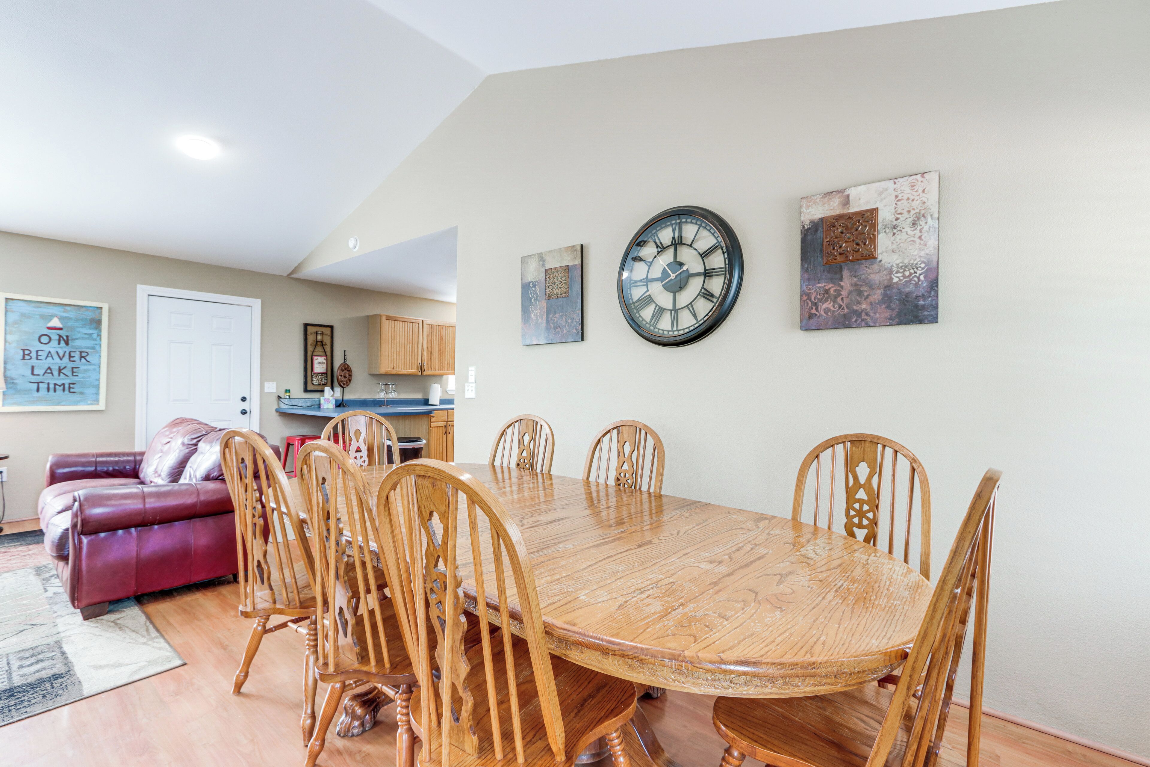 A dining area with a wooden table and chairs, a clock on the wall, and a red couch in the background.