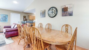 A dining area with a wooden table and chairs, a clock on the wall, and a red couch in the background.