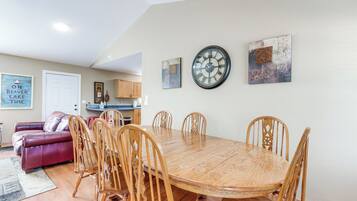 A dining area with a wooden table and chairs, a clock on the wall, and a red couch in the background.