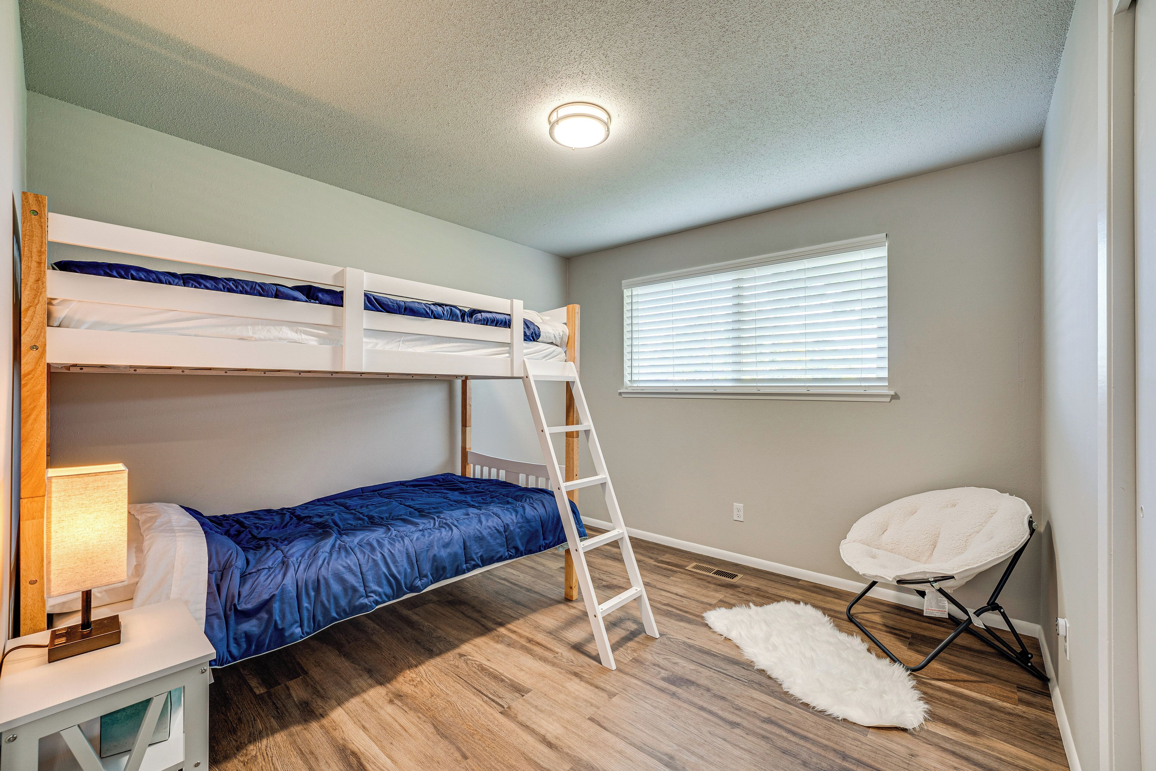 Habitación con literas, una escalera, un escritorio con lámpara, un felpudo blanco y una silla blanca.