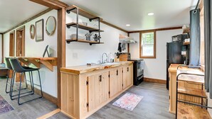A modern kitchen with wooden cabinets, a central island, and built-in shelves. - Cozy Catskills Cabin - 12 Mi to Windham Mountain! (East Durham)