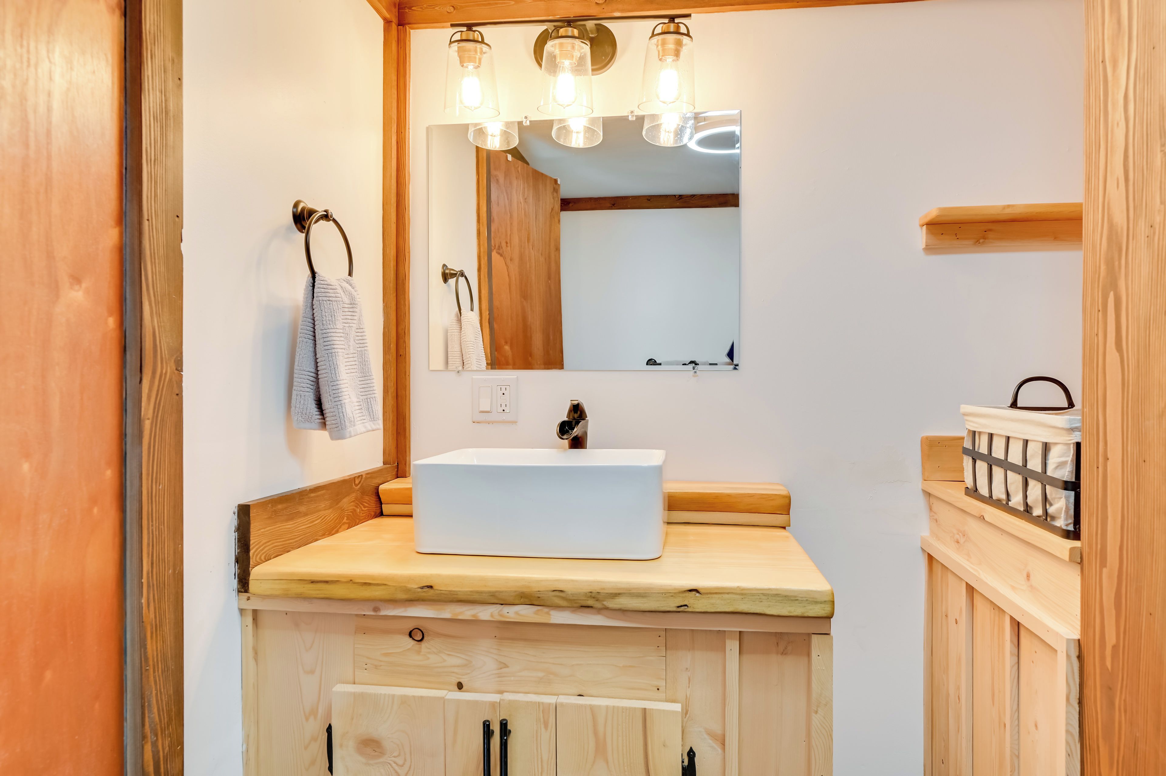 A wooden bathroom with a white sink, a mirror, and three light fixtures above it.