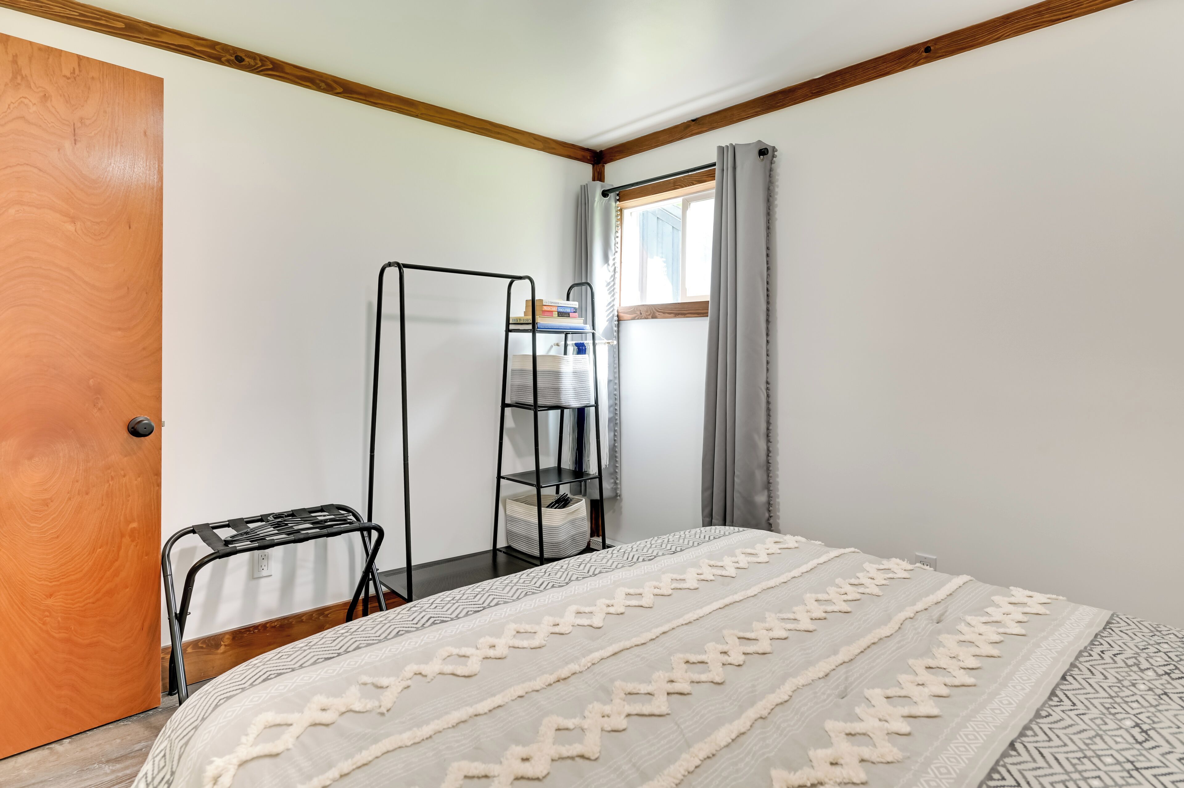 Quarto com uma cama, porta de madeira, estante de metal e janela com cortinas.