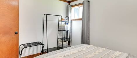 Quarto com uma cama, porta de madeira, estante de metal e janela com cortinas.