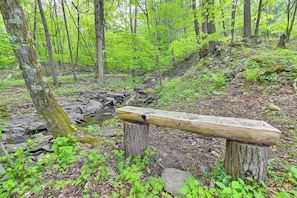 Eine hölzerne Bank in einer bewaldeten Gegend mit einem Bach und Felsen.