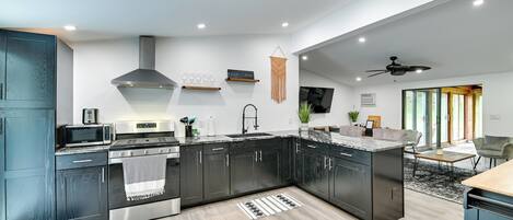 Une cuisine moderne avec des meubles de couleur sombre, un four à micro-ondes, une cuisinière et une décoration murale en macramé suspendue.