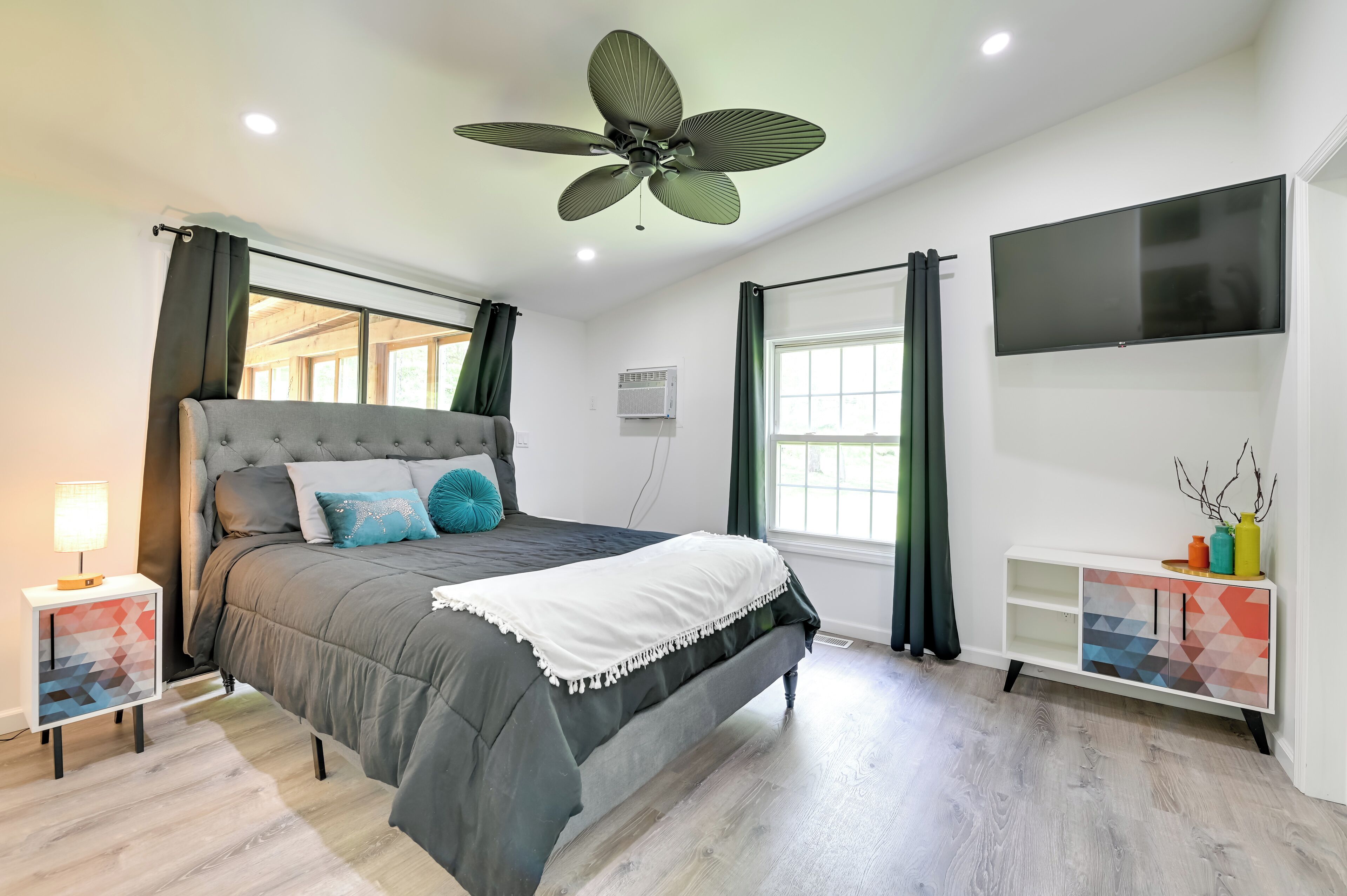 Un dormitorio moderno con una cama grande, un ventilador de techo, un televisor y una ventana con cortinas.
