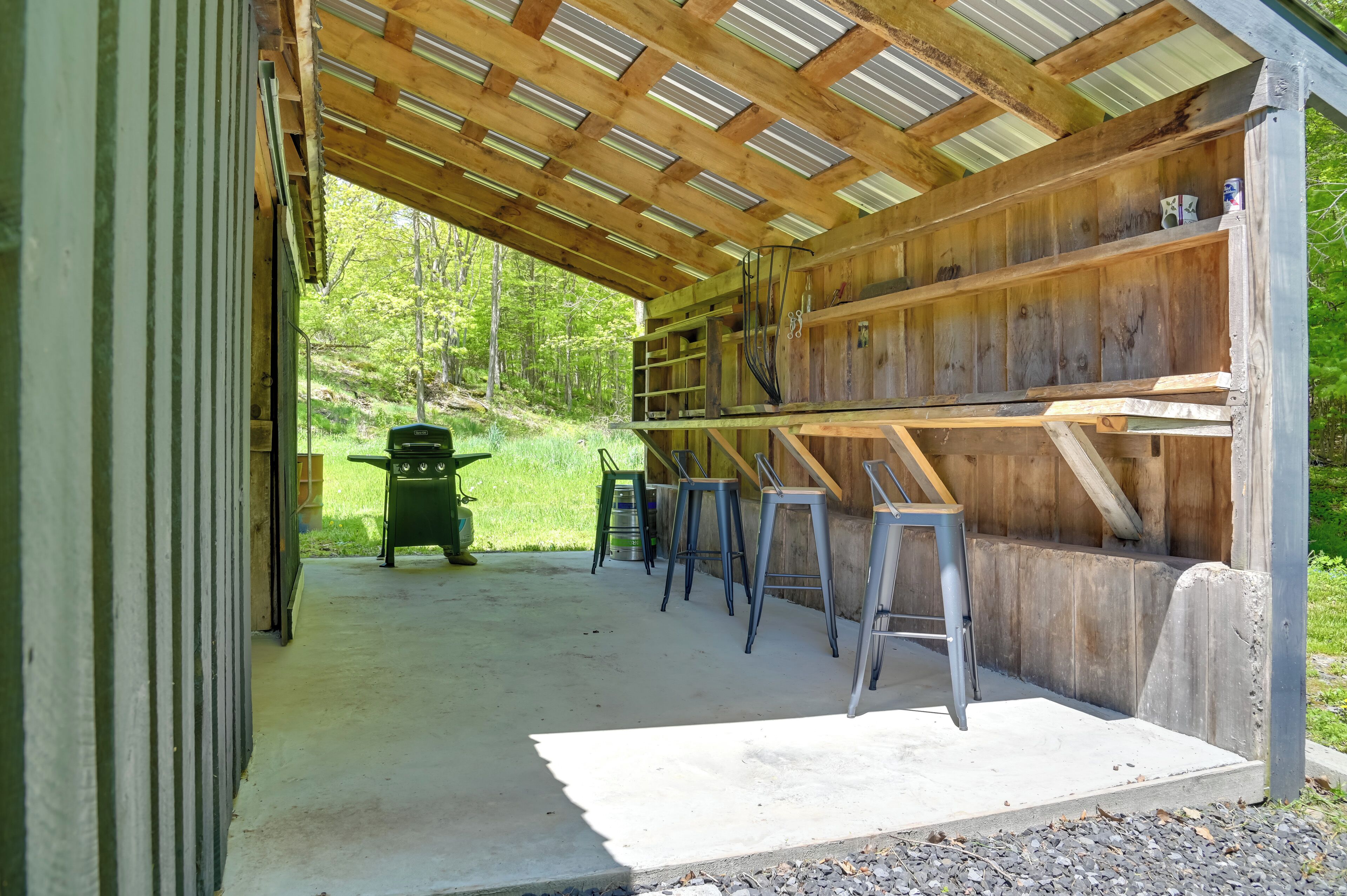 A covered outdoor area with a concrete floor, wooden benches, and metal stools.