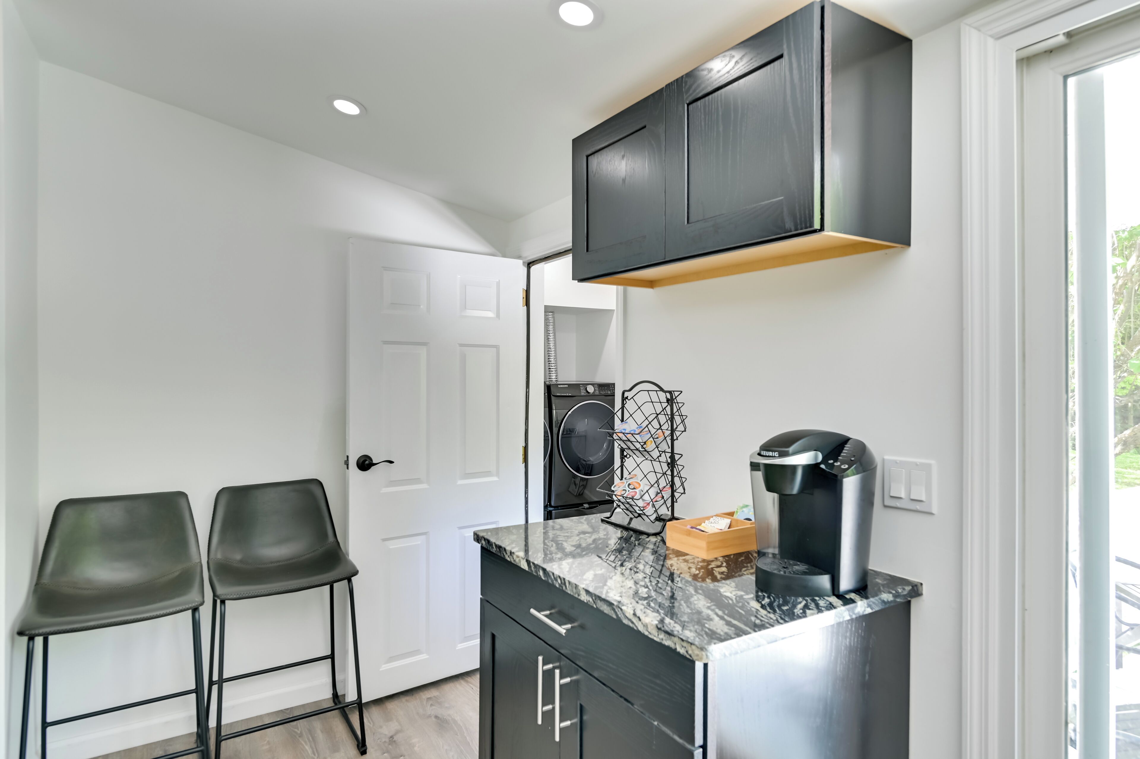 A compact kitchen with a built-in washer and dryer, a coffee machine, and two bar stools.