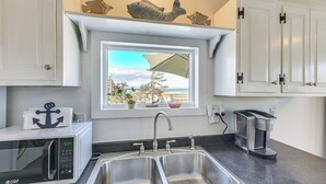 A kitchen with a double sink, a microwave, a coffee maker, and a window with a view of the ocean. - Peaceful Lubec Home w/ Views: Walk to Beach! (Lubec)