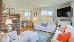 A living room with a brick wall, white furniture, a fireplace, and a view of the outdoors. - Peaceful Lubec Home w/ Views: Walk to Beach! (Lubec)