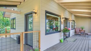 A covered porch with a wooden deck, large windows, and outdoor seating.