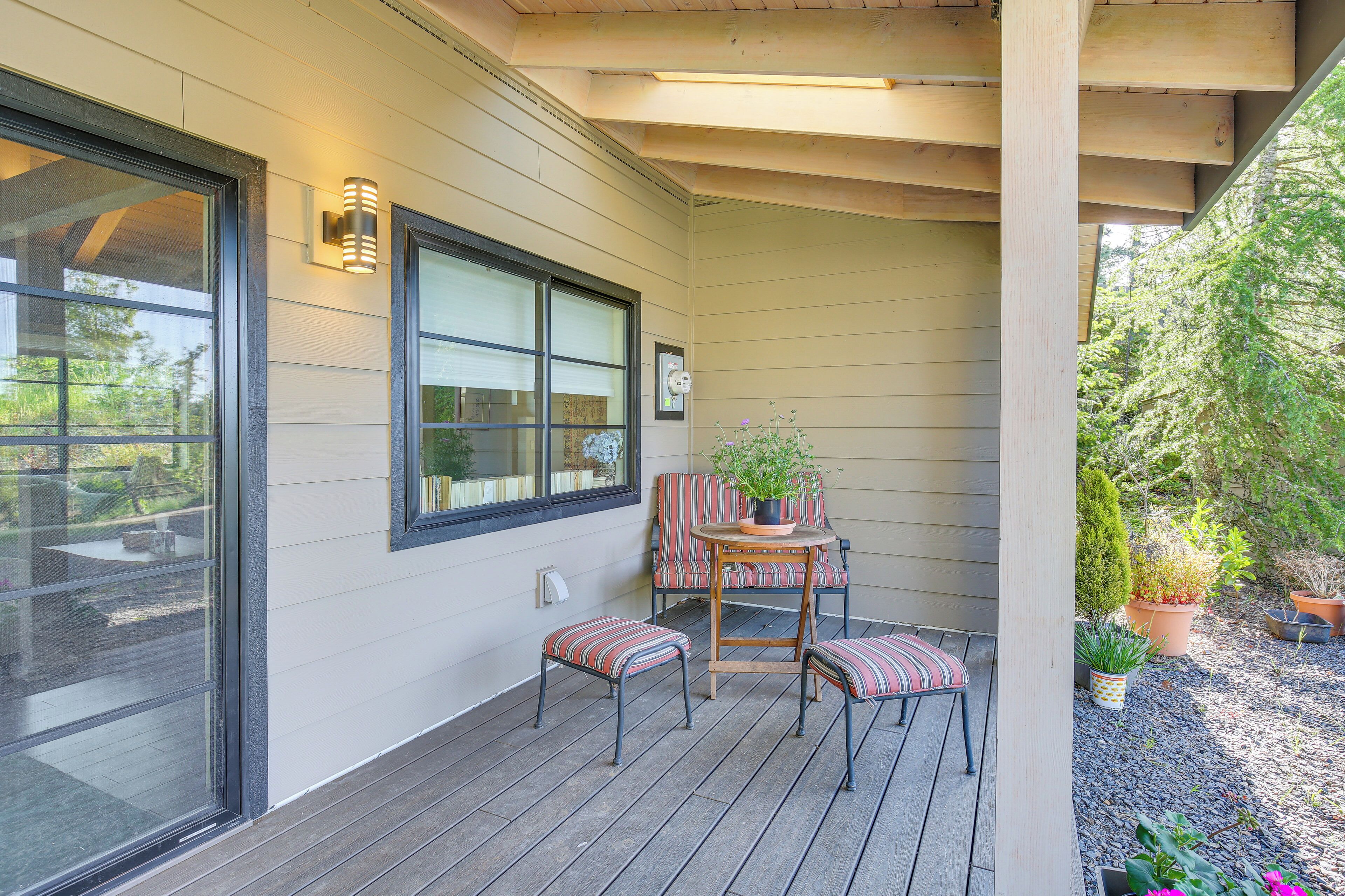 A covered outdoor seating area with a table and chairs, a potted plant, and a window.