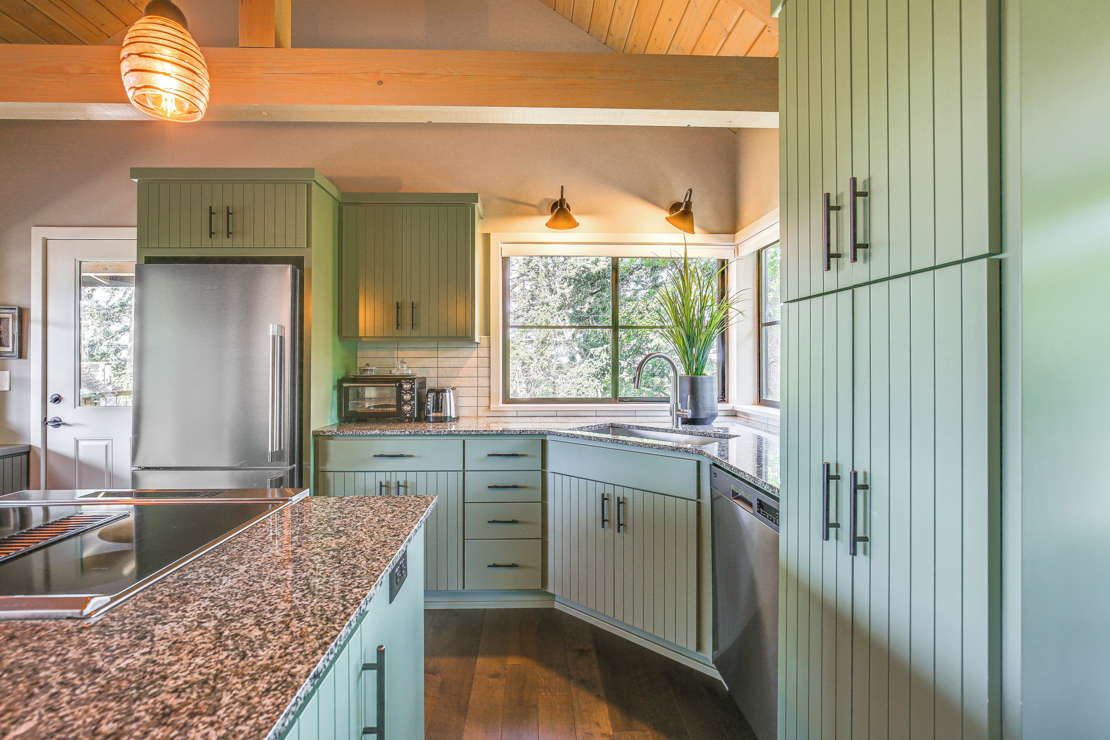 Een moderne keuken met groene kastjes, een roestvrijstalen koelkast, een ingebouwde oven en een granieten aanrecht.