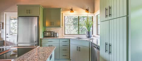 A modern kitchen with green cabinets, a stainless steel refrigerator, a built-in oven, and a granite countertop.