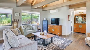 A spacious living room with a high ceiling, large windows, a wooden entertainment center, and a cozy seating area.