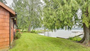 A wooden cabin with a grassy yard and a dock extending into a lake. - Waterfront Grapeview Escape w/ Boat Dock & Views! (Grapeview)
