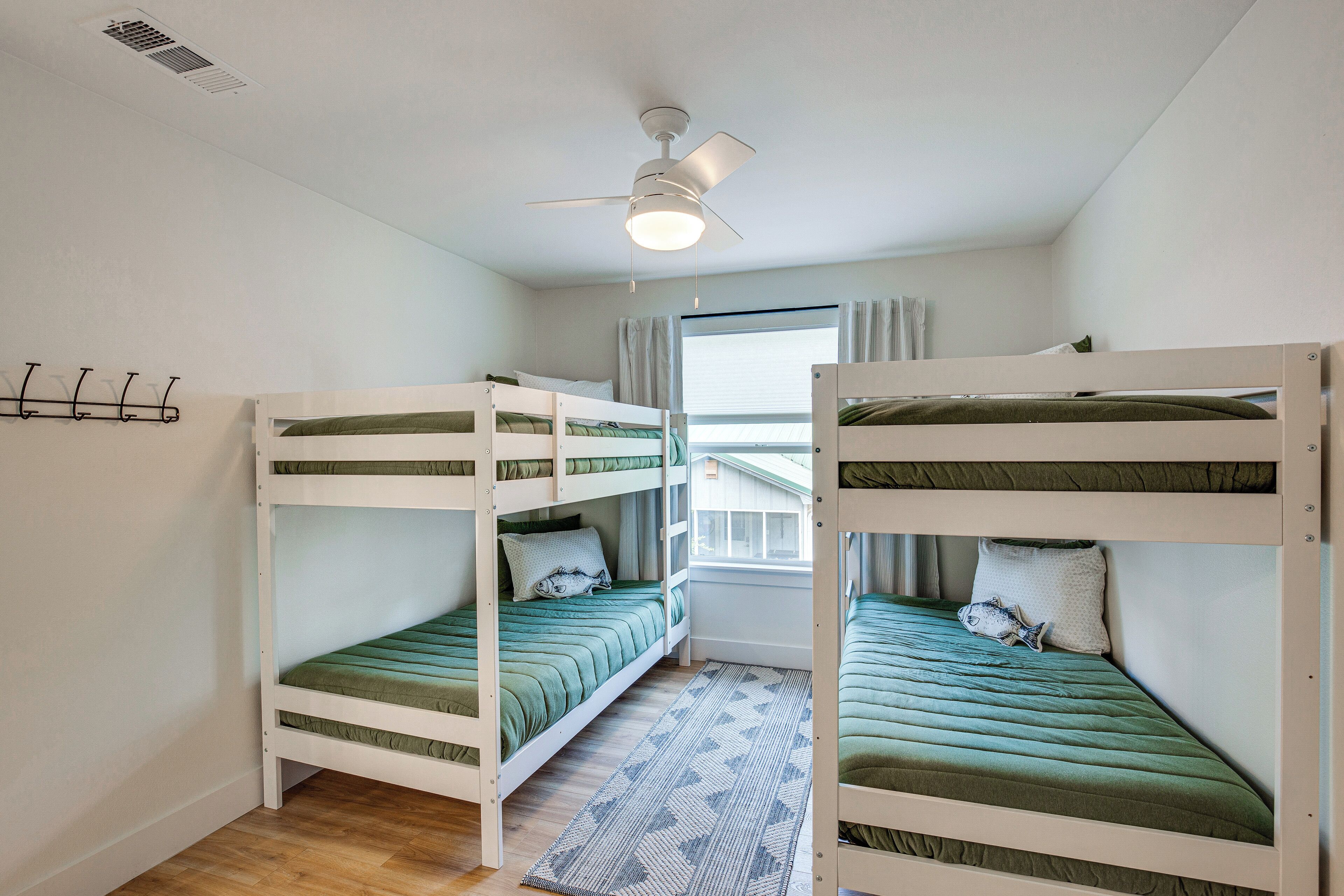 A room with bunk beds, a ceiling fan, a window with curtains, and a patterned rug.