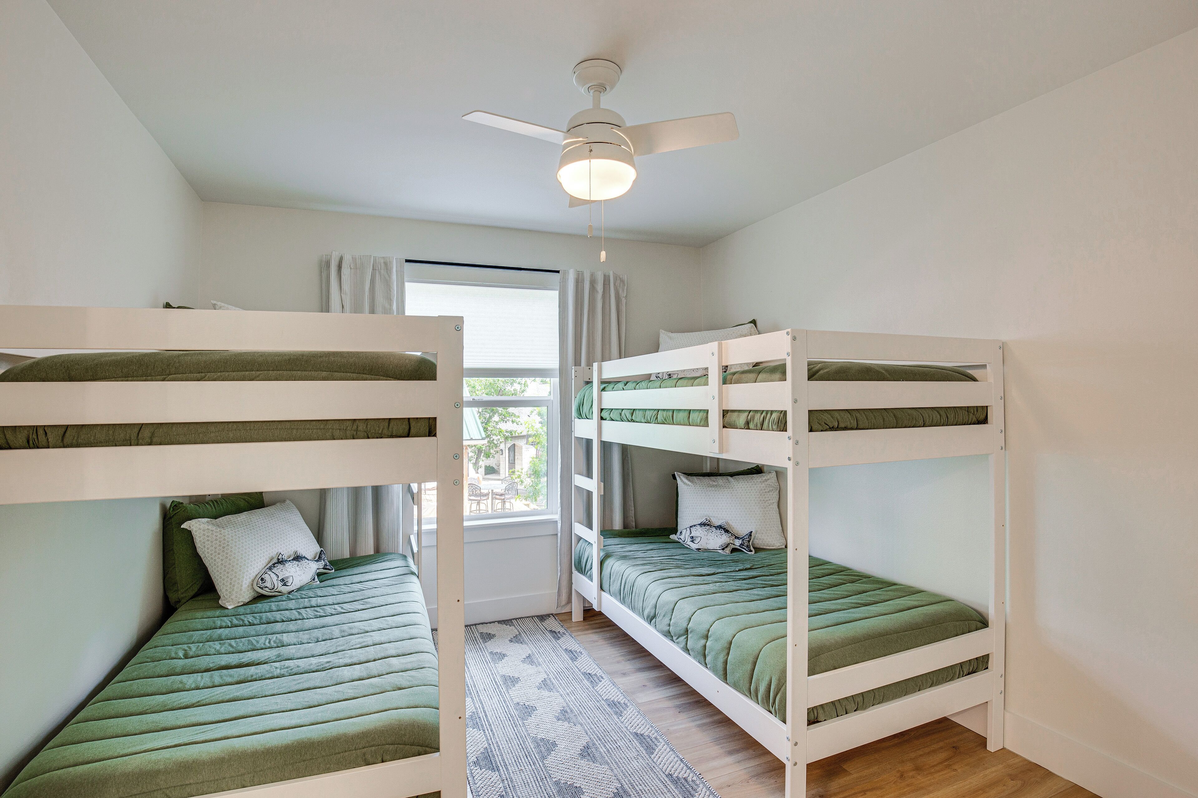Une chambre avec des lits superposés, un ventilateur de plafond et une fenêtre avec des rideaux.