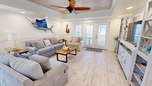 Ein geräumiges Wohnzimmer mit grauem Sofa, einem Holztisch und einem Deckenventilator.