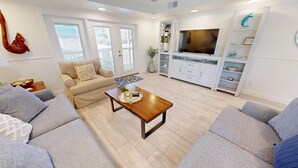 Ein modernes Wohnzimmer mit einem beige farbenen Sofa, einem Holztisch und einem Fernseher auf einem weißen Schrank.