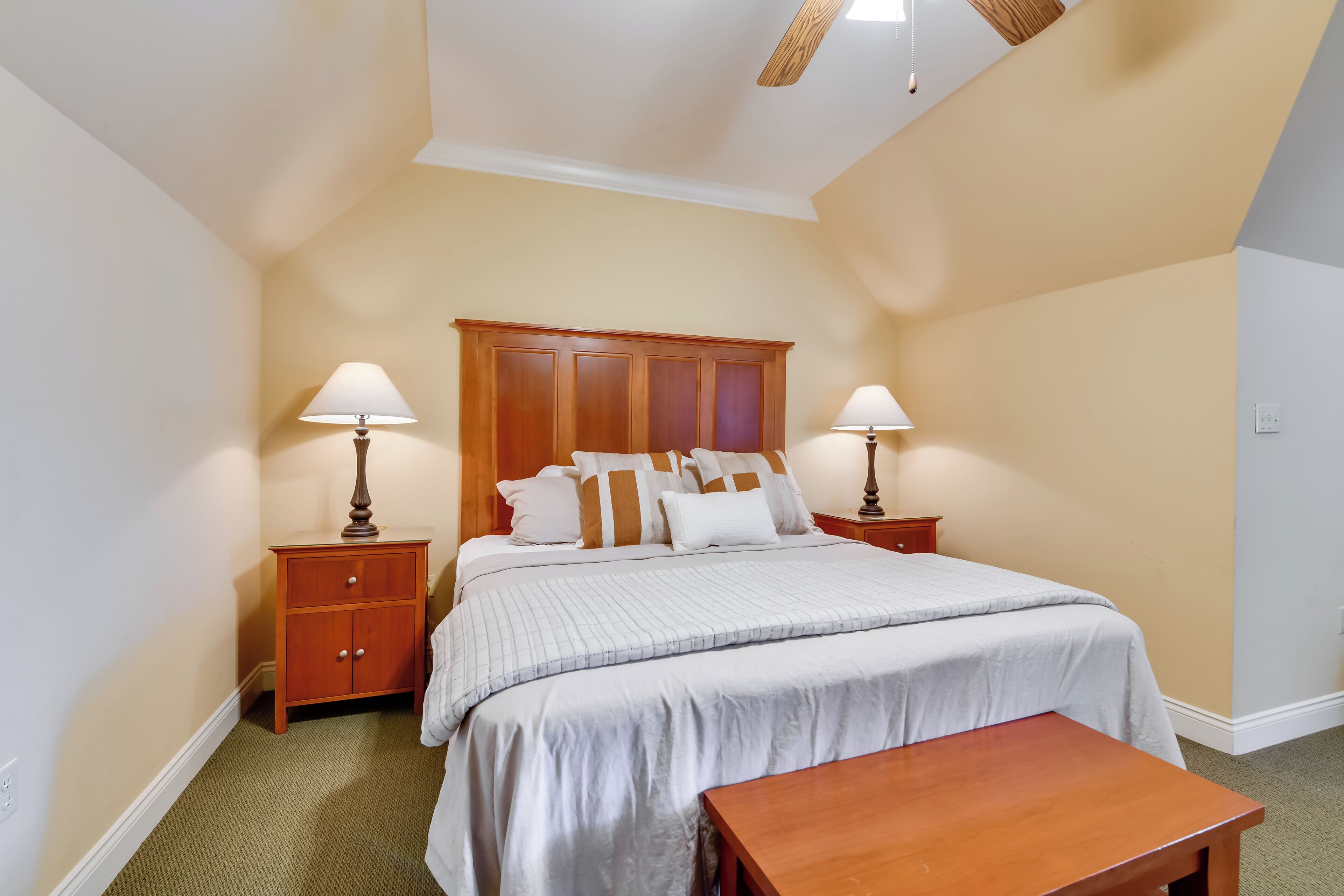 Quarto com cama, mesas de cabeceira, um banco de madeira e ventilador de teto.