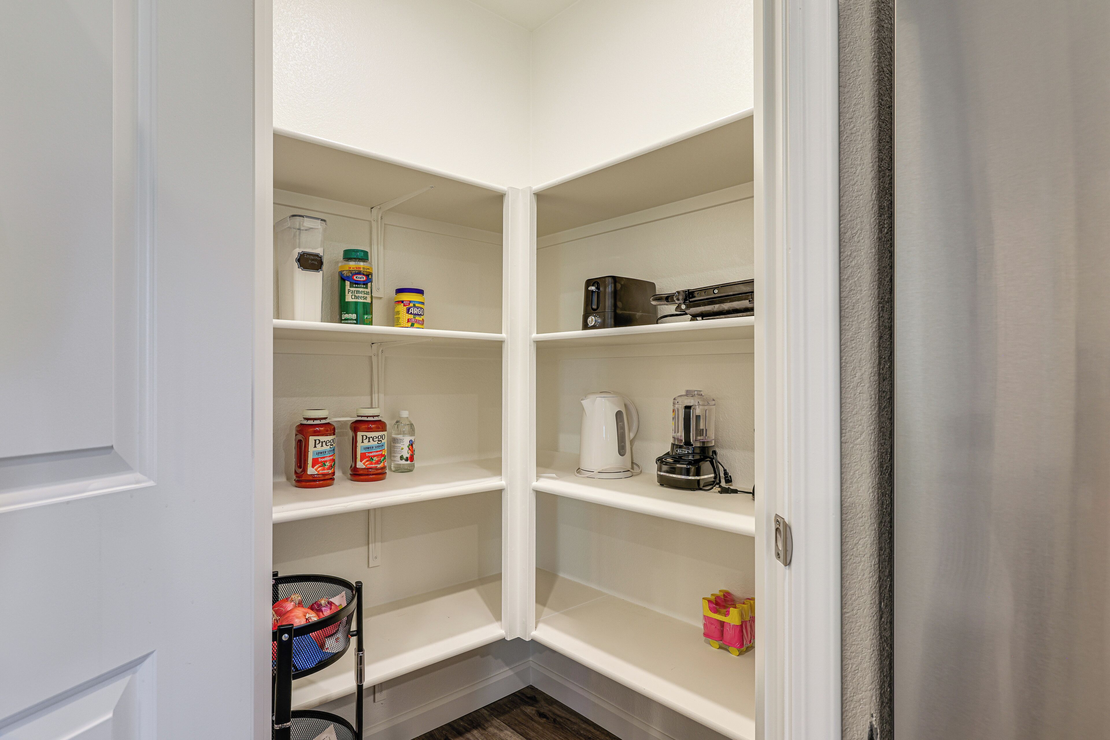 A narrow pantry with white shelves, containing various food items and kitchen appliances.