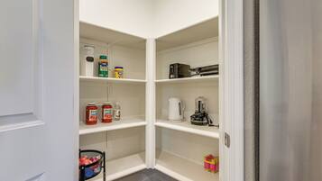 A narrow pantry with white shelves, containing various food items and kitchen appliances.