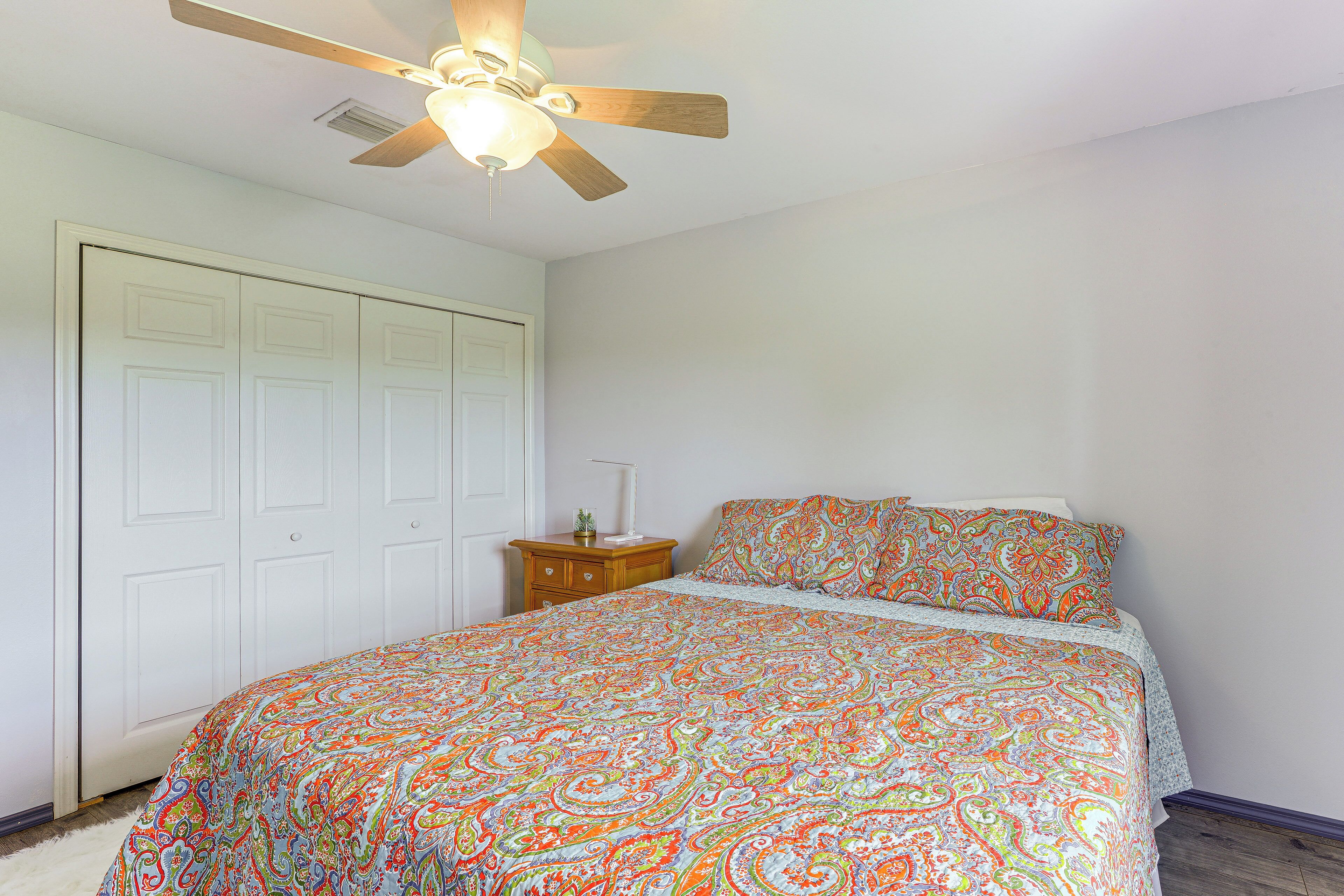 A bedroom with a bed, a ceiling fan, and a nightstand with a lamp.