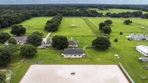 An equestrian arena surrounded by green fields and trees, with a stable and buildings nearby. - Idyllic Anthony Home: Riding Arena w/ Mirror Wall! (Anthony)