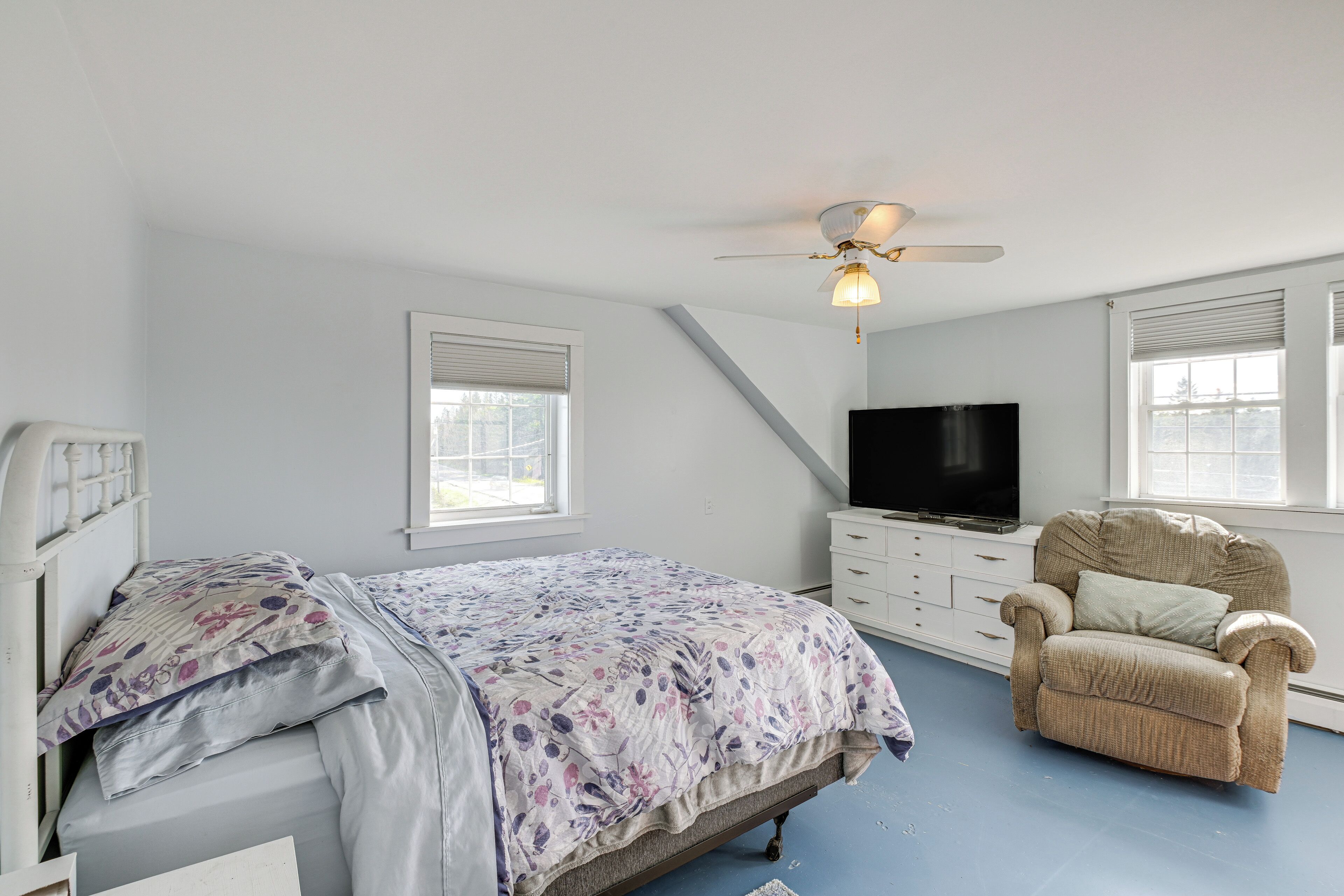 A bedroom with a bed, a chair, a TV, and a ceiling fan.
