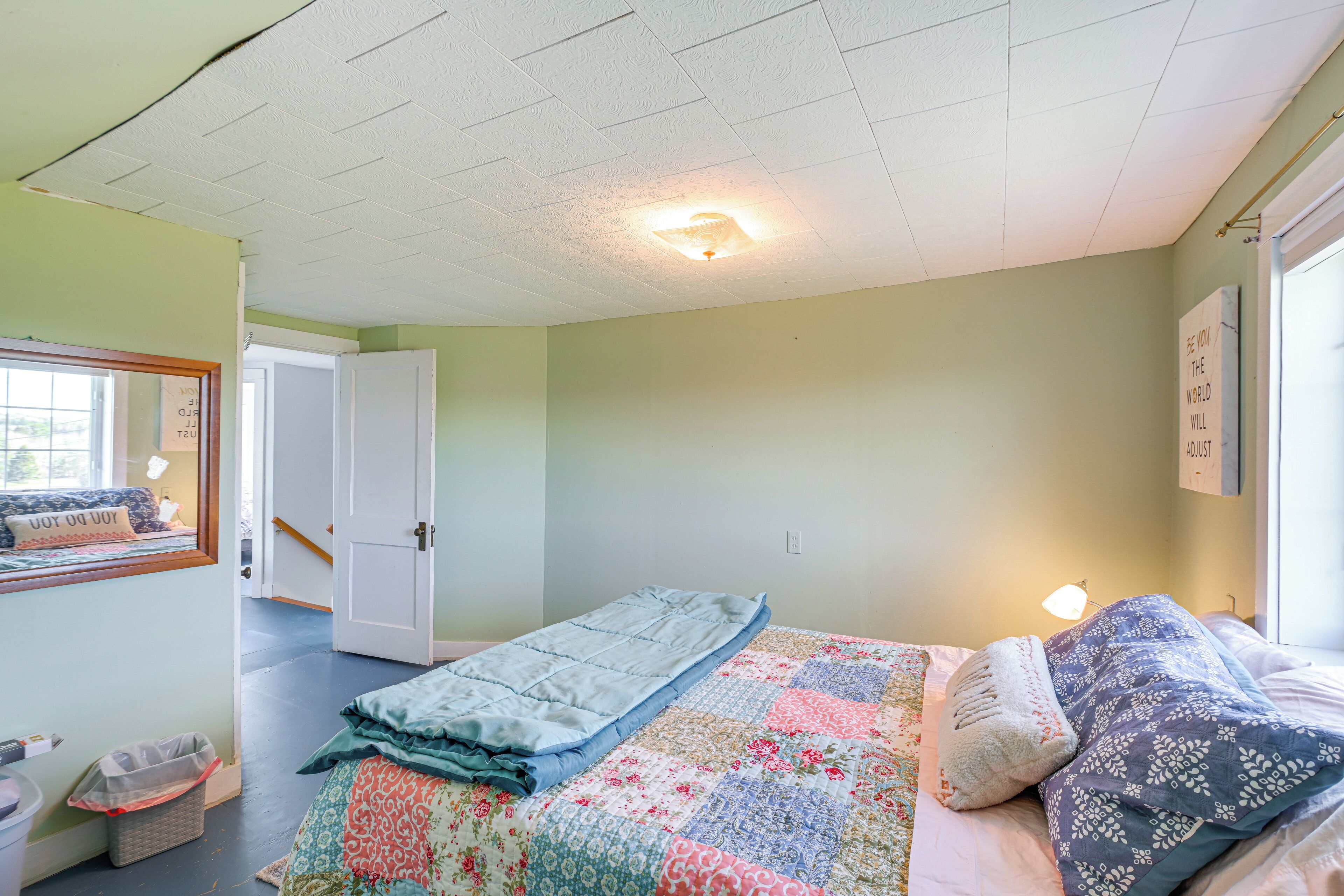 A bedroom with a bed, a window, a door, and a ceiling light.