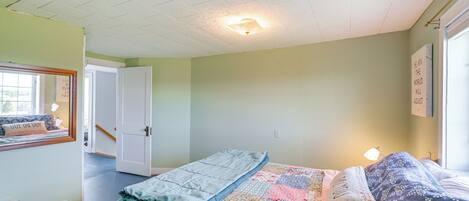 A bedroom with a bed, a window, a door, and a ceiling light.