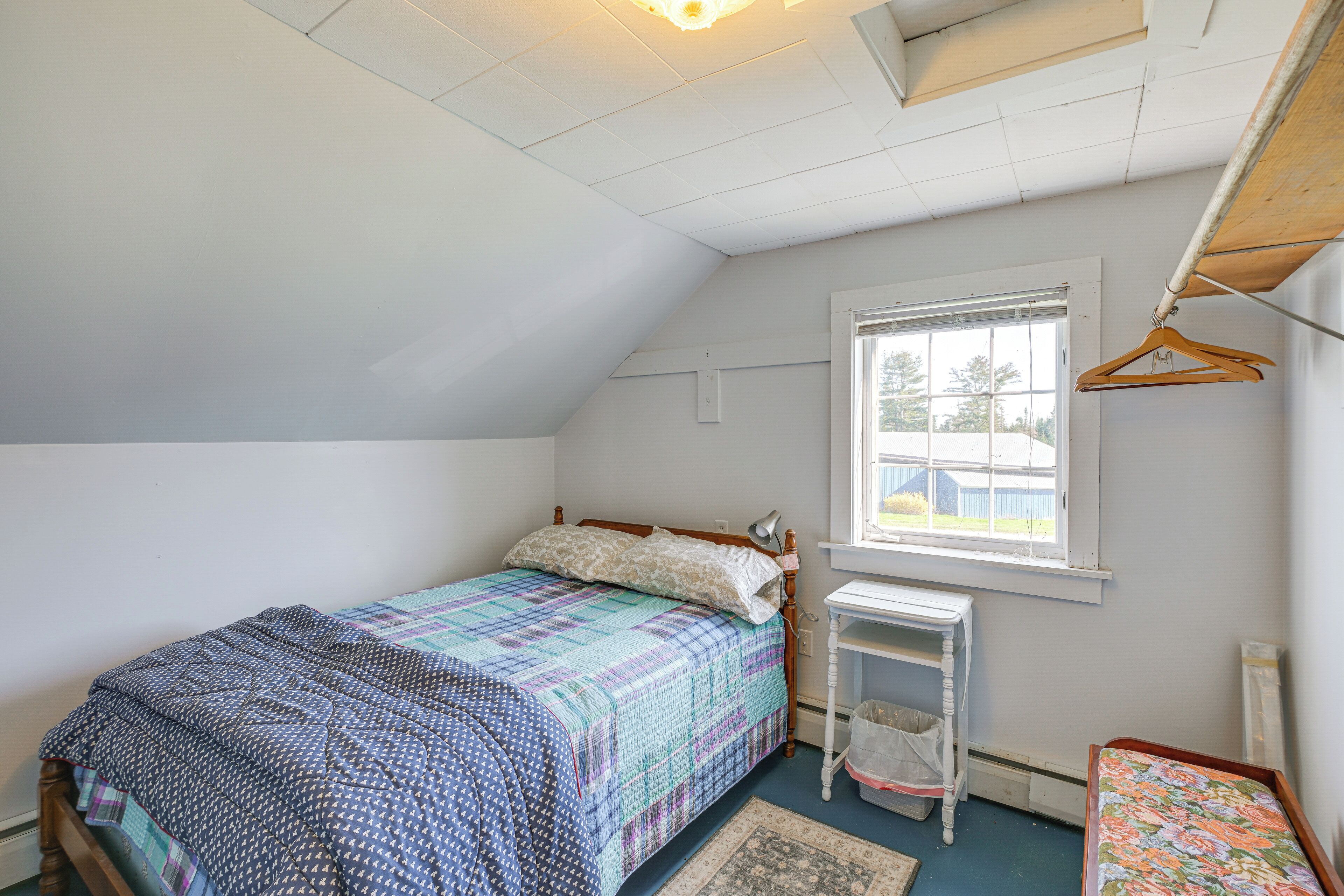 A bedroom with a bed, a window, a desk, and a hanging clothes rack.