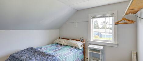 Ein Schlafzimmer mit Bett, Fenster, Schreibtisch und einer Kleiderstange.