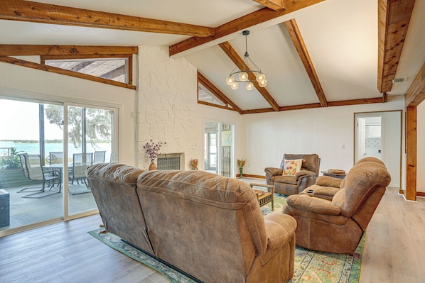 A spacious living room with a large brown leather sofa, a wooden ceiling with exposed beams, and a large sliding glass door leading to an outdoor area.