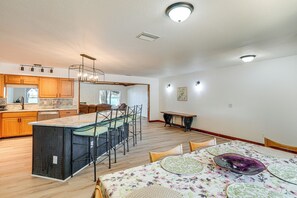 A spacious kitchen with wooden cabinets, a central island, and a dining area with a floral tablecloth.