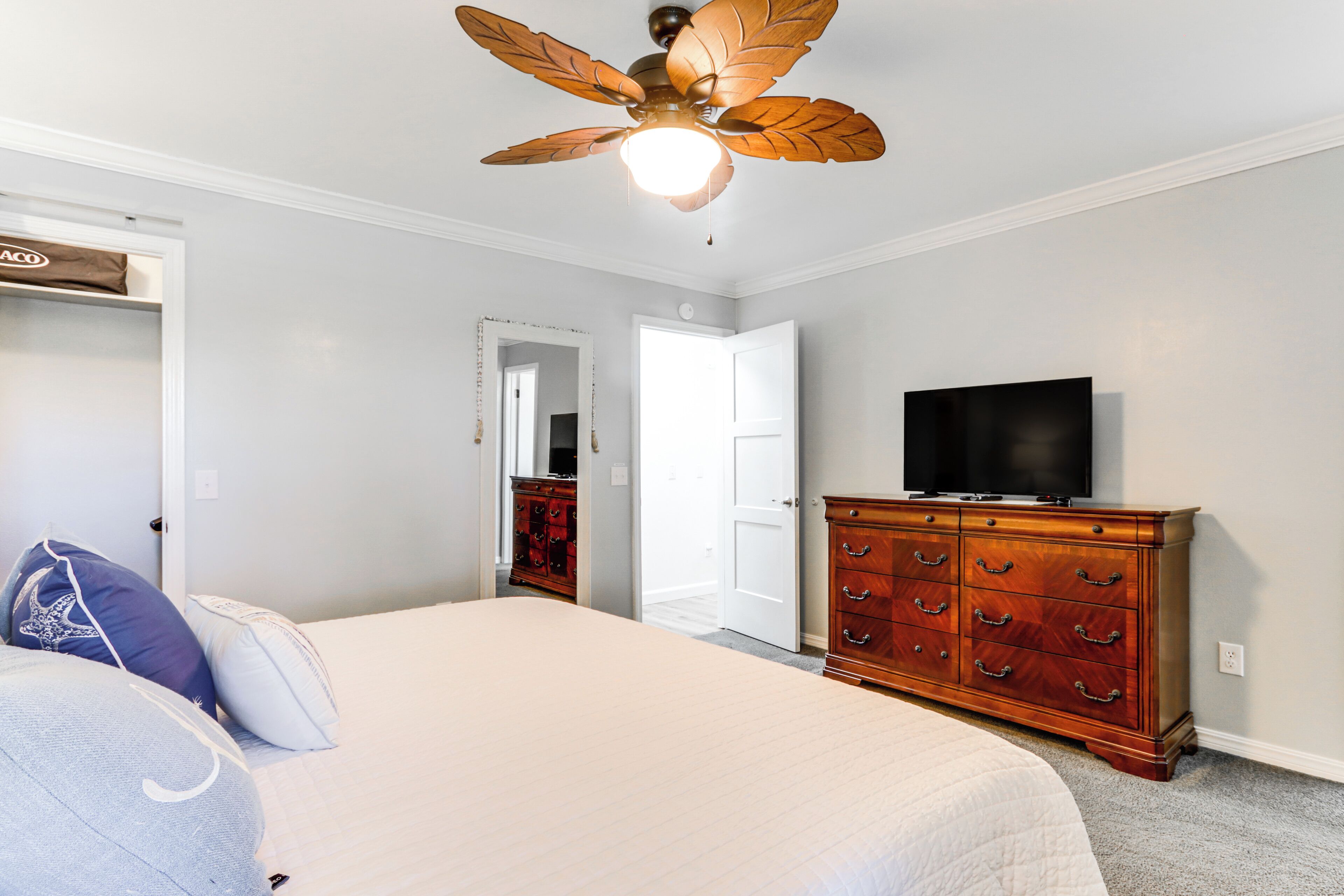 A bedroom with a bed, a dresser, a television, and a ceiling fan.
