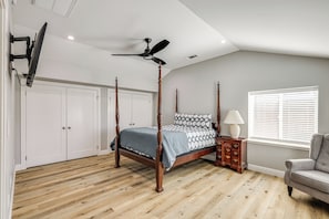 A four-poster bed with a wooden frame and a gray bedspread, a ceiling fan, a window with blinds, and a wooden nightstand with drawers. - Quaint Hughson Vacation Rental, Walk to Downtown! (Hughson)
